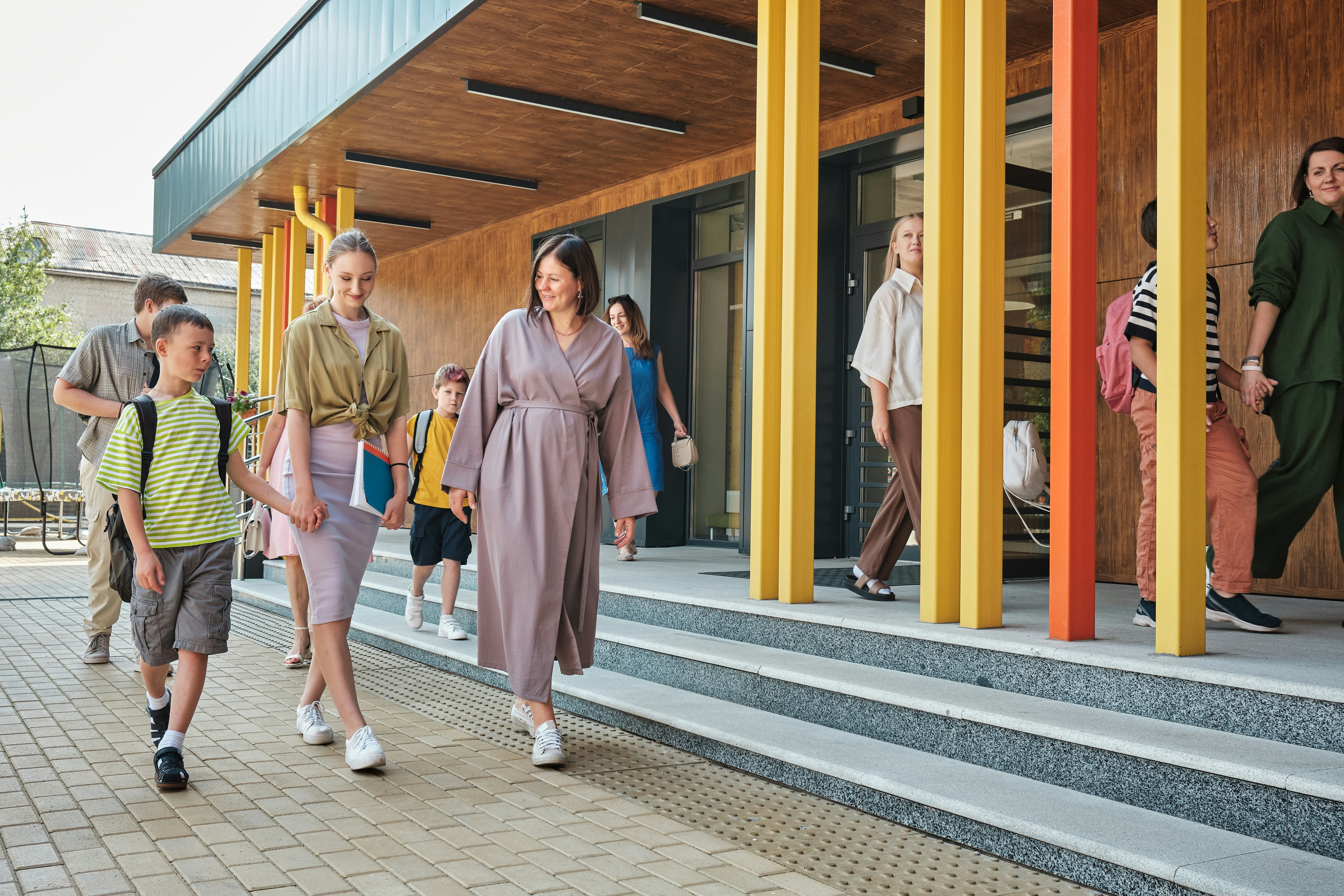 Supportive school staff walking alongside elementary students in a warm, sunlit courtyard